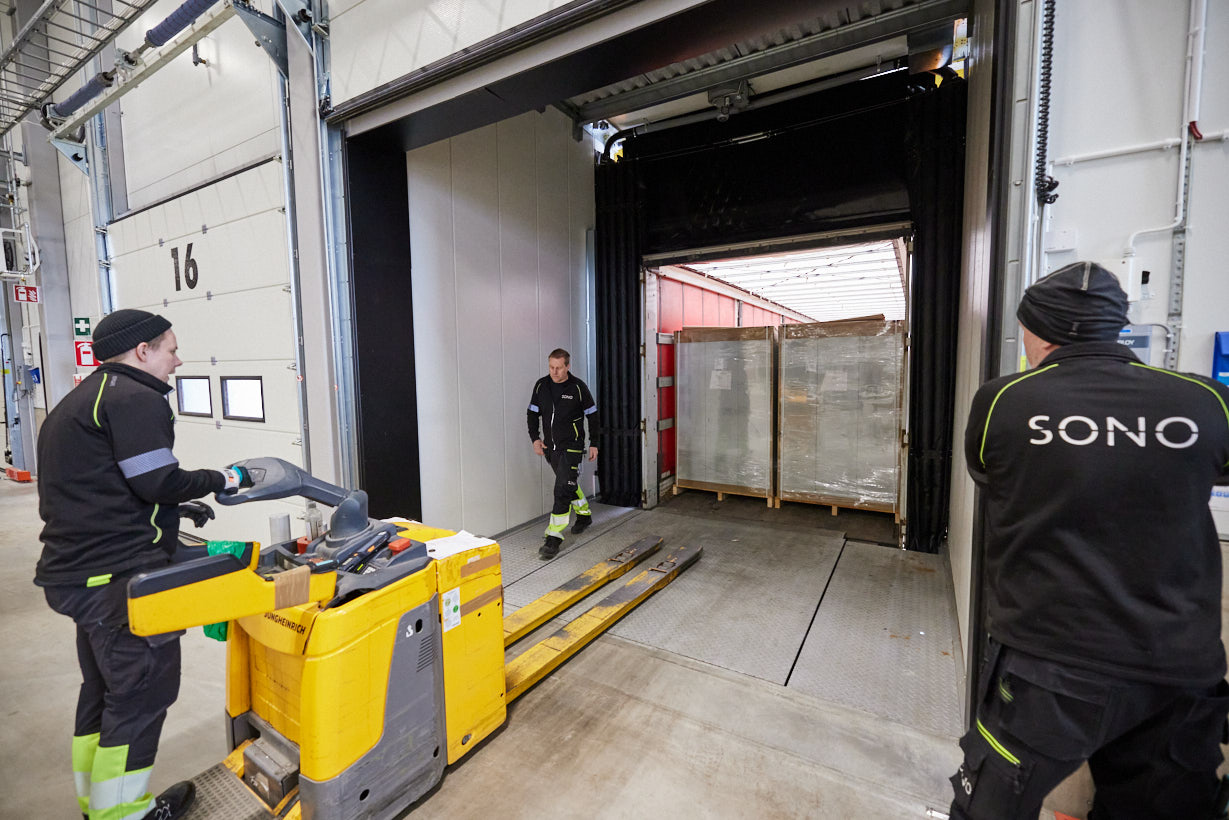 En truck og truckfører laster på en lastebil via en port på lageret.